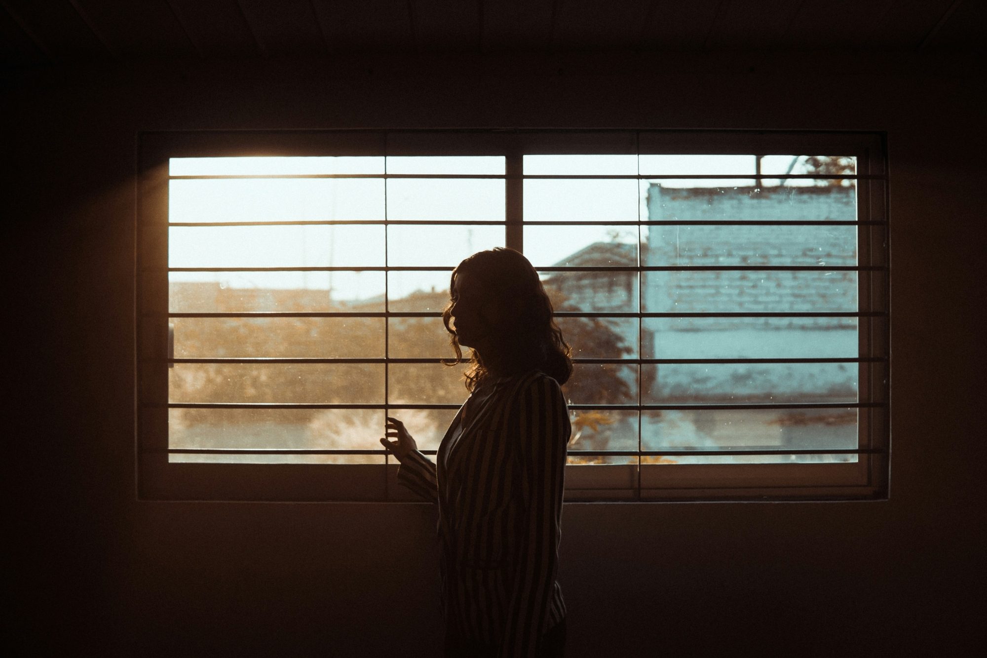 Une femme en contre jour regarde par la fenêtre